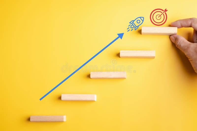 Wooden blocks arranged as steps with an ascending arrow and rocket leading to a target symbolizing achievement and progress