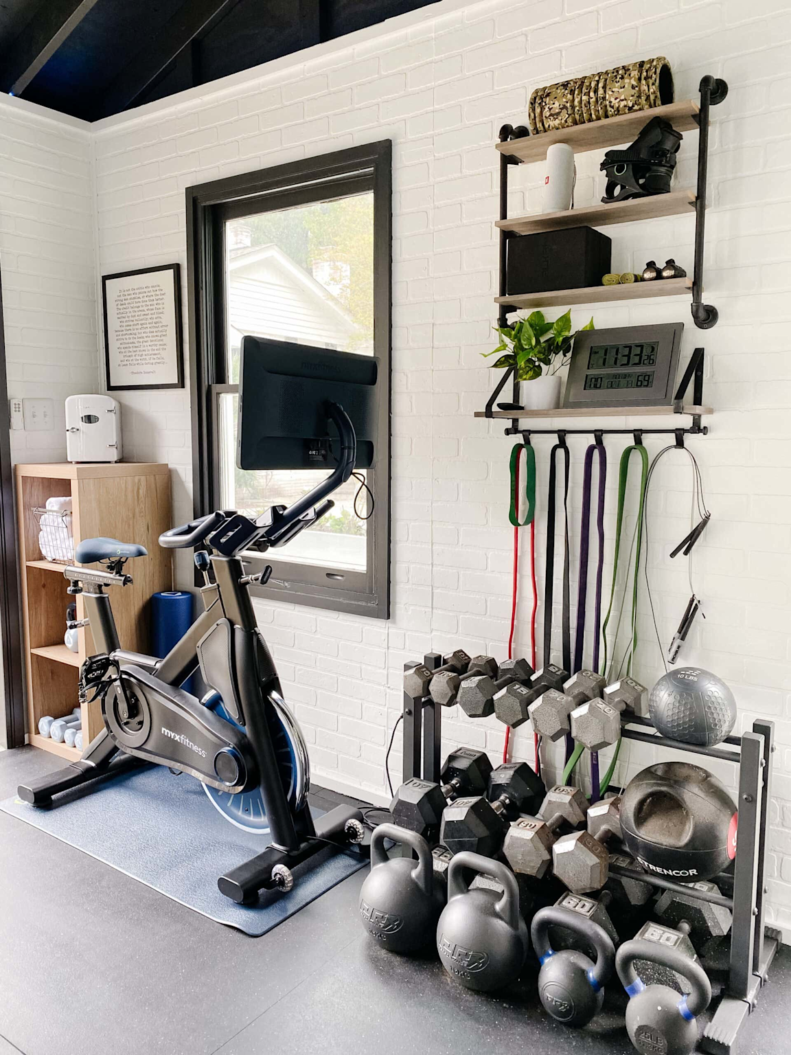 Organized home gym space with kettlebells, dumbbells, resistance bands, and a stationary bike in a bright room