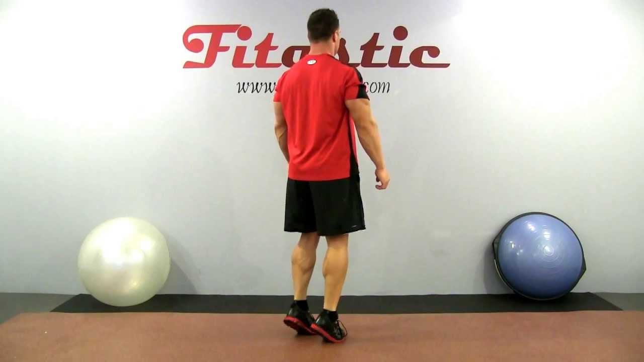 Man performing a standing bodyweight calf raise in a gym setting demonstrating proper posture for calf muscle training without equipment