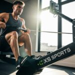 XS Sports Rowing Machine: Complete Review & Guide Fit male athlete performing rowing exercise on XS Sports branded rowing machine in contemporary fitness facility with natural lighting from floor-to-ceiling windows